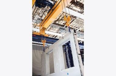 Double girder travelling crane in tandem control system lifts precast concrete part of the company Benders Sverige