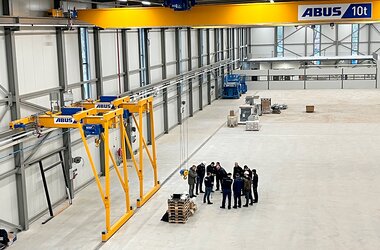 Two semi-goliath cranes in a factory hall, with an overhead travelling crane on an upper level.