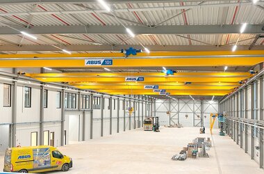 An industrial hall with several overhead travelling cranes on one track, with an ABUS service vehicle in the foreground.