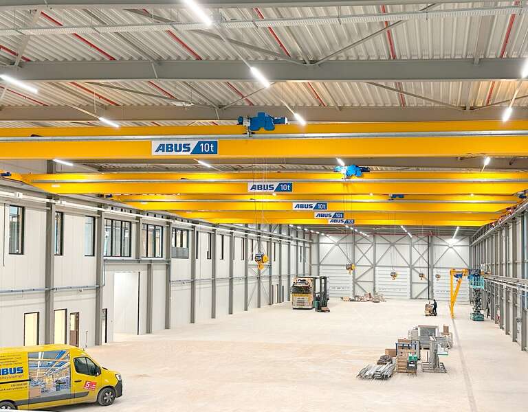 An industrial hall with several overhead travelling cranes on one track, with an ABUS service vehicle in the foreground.