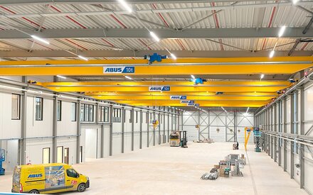 An industrial hall with several overhead travelling cranes on one track, with an ABUS service vehicle in the foreground.
