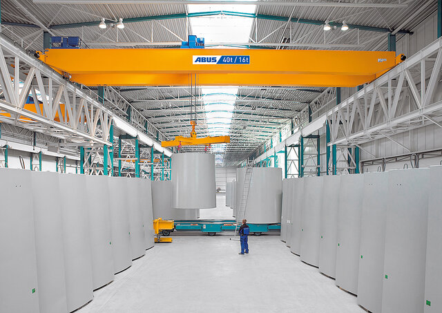 An overhead travelling crane in an industrial hall is moving heavy loads whilst an employee is standing in the operating range.