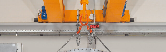 A crane's end carriage with extension sections, to which a chain sling carrying a load is attached.