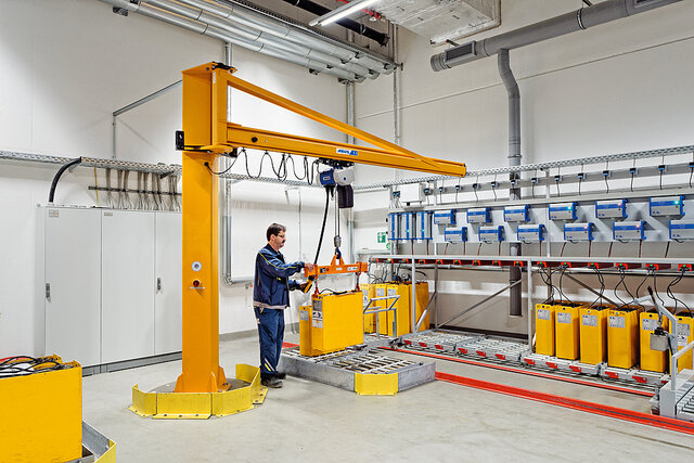 An employee operates a column-mounted jib crane and moves a load at a workstation in an industrial hall
