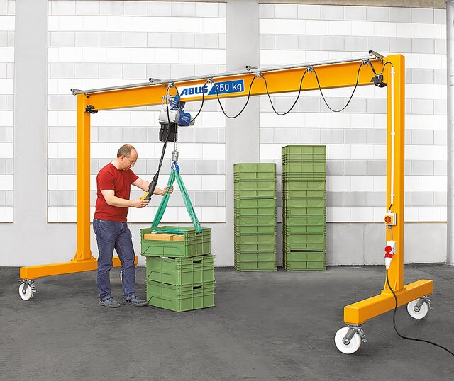 An employee operates a suspended rail system with a chain hoist and moves a load around a workshop