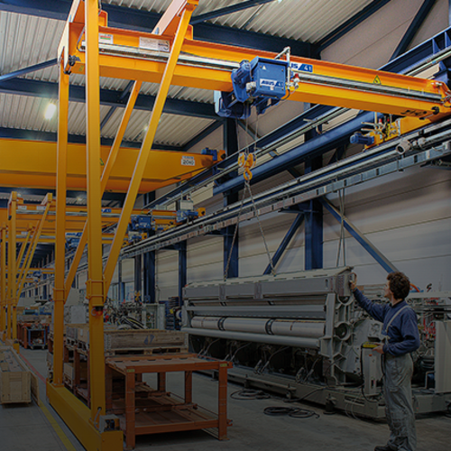 ABUS semi-goliath crane in an industrial hall with a load capacity of up to 10 tonnes and a span of up to 15 metres, designed for flexible material handling at workstations.